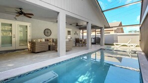 Un espace piscine extérieur abrité, doté d’un ventilateur de plafond, de sièges et d’une table à manger.