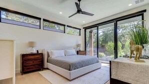 Een moderne slaapkamer met een groot bed, een plafondventilator en uitzicht op de omgeving door grote ramen.