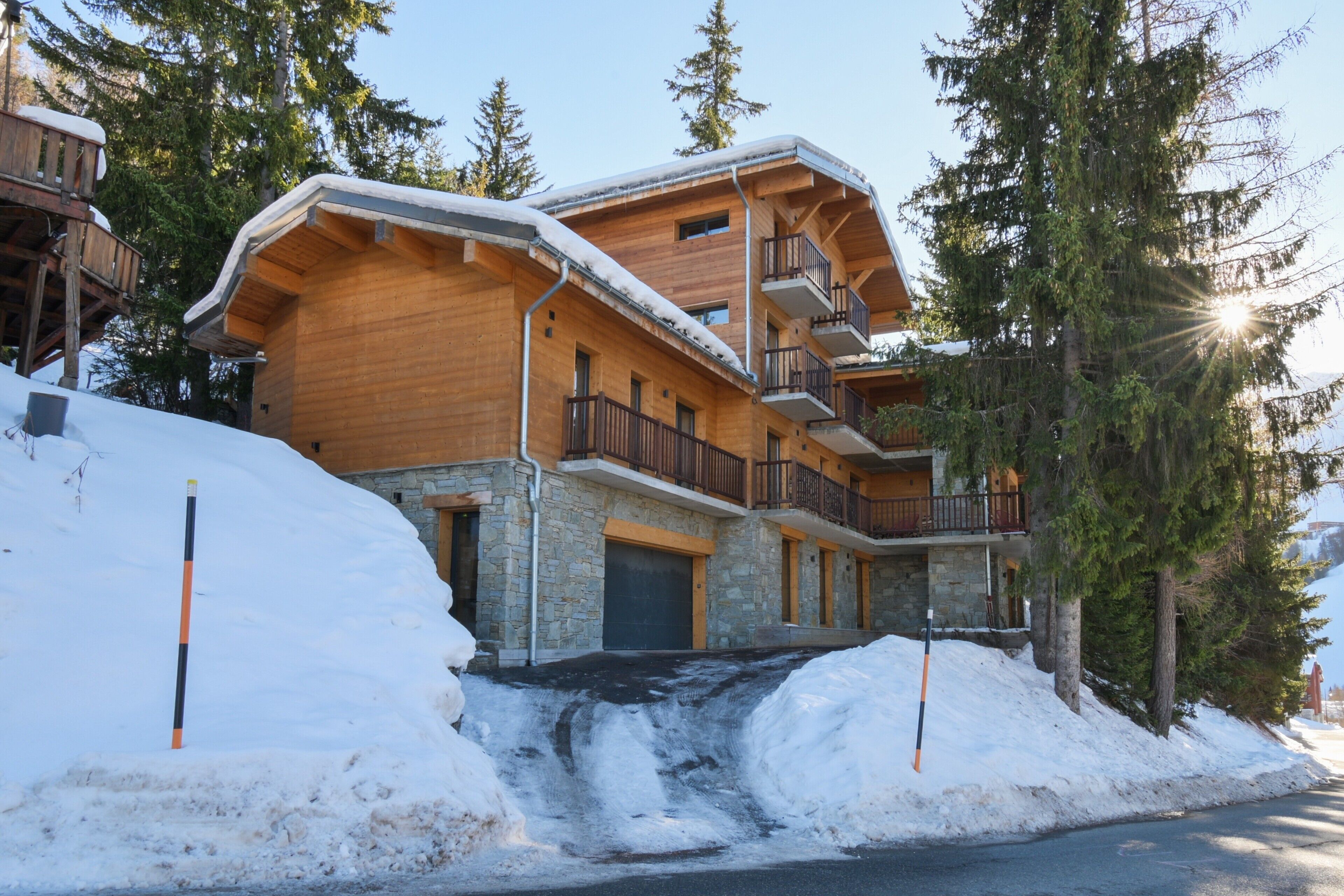 Un chalet en bois doté de balcons, avec une fondation en pierre et une allée enneigée.