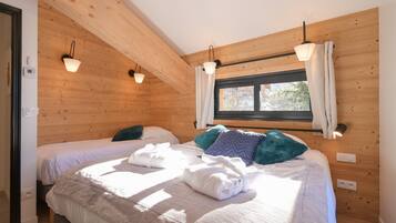 A room with wooden walls, two beds, a window with curtains, and wall-mounted lights.