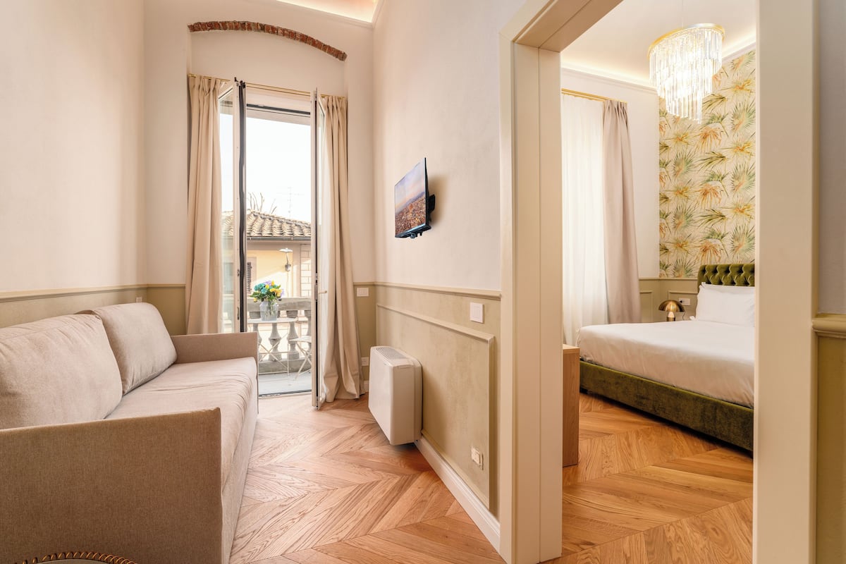 Habitación de hotel con sofá, cama, radiador, televisor y vista al balcón exterior.