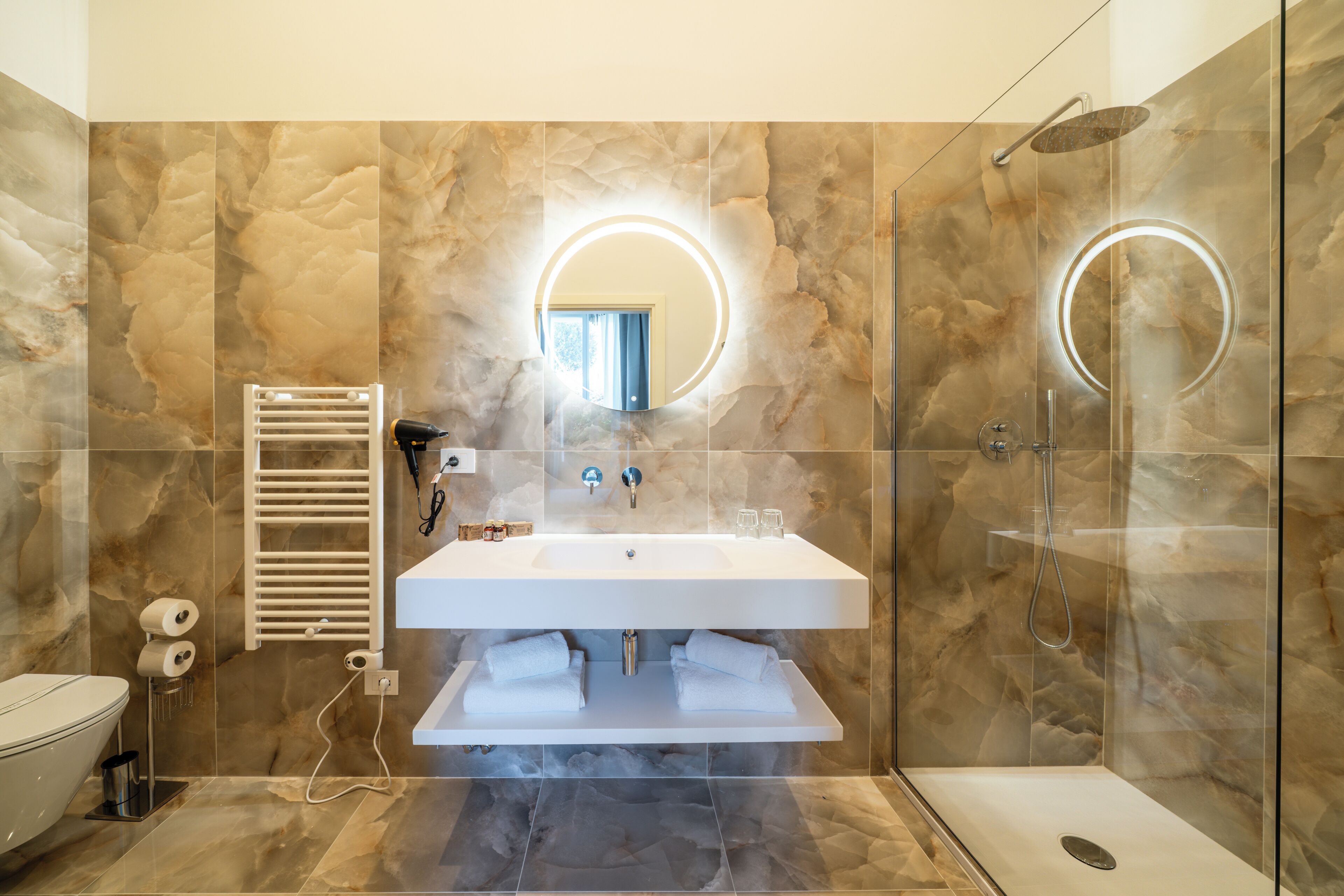 A modern bathroom with a marble wall, a white sink, a glass-enclosed shower, and a towel rack.