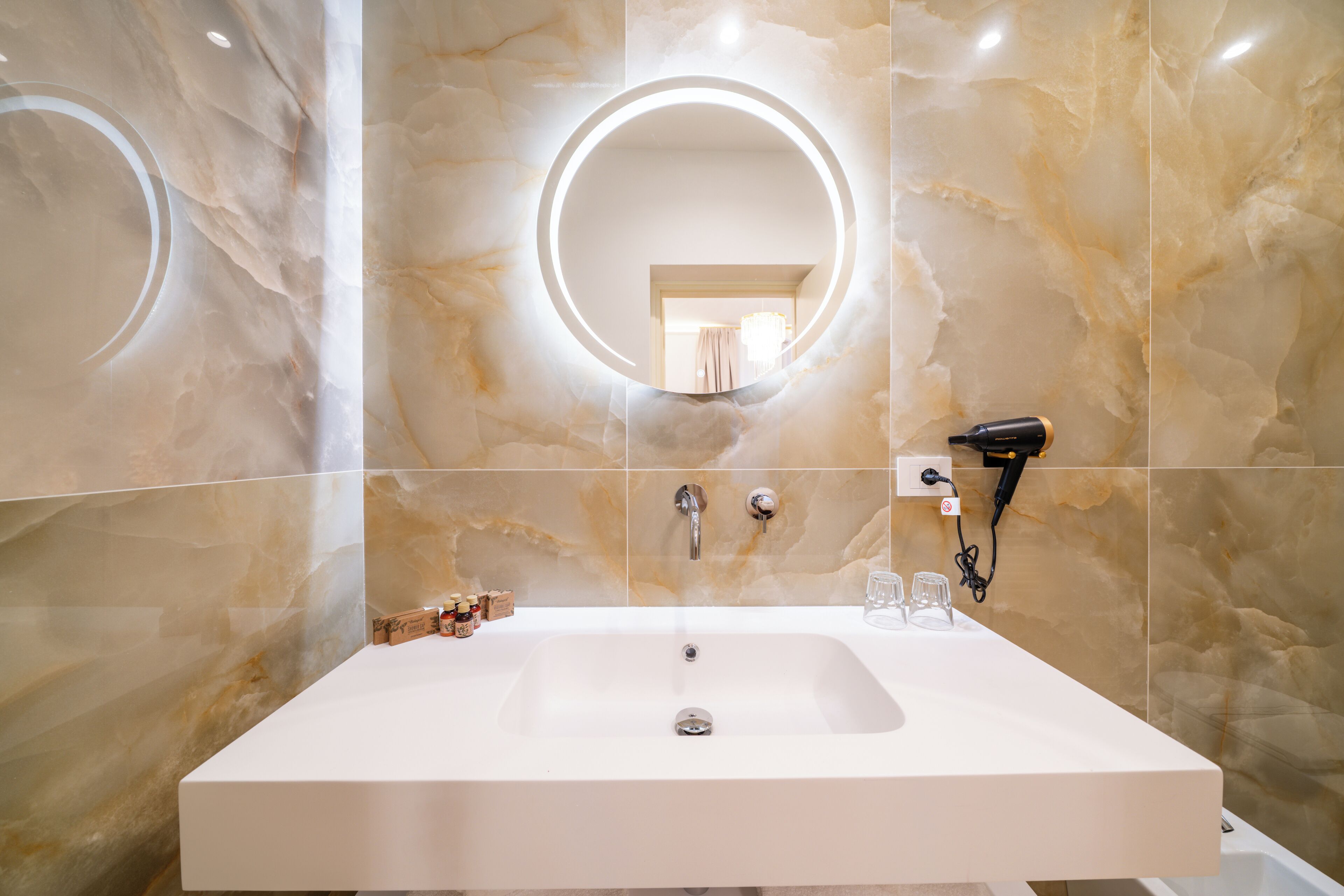 A modern bathroom with a large sink, a round mirror, and a hairdryer on the wall.