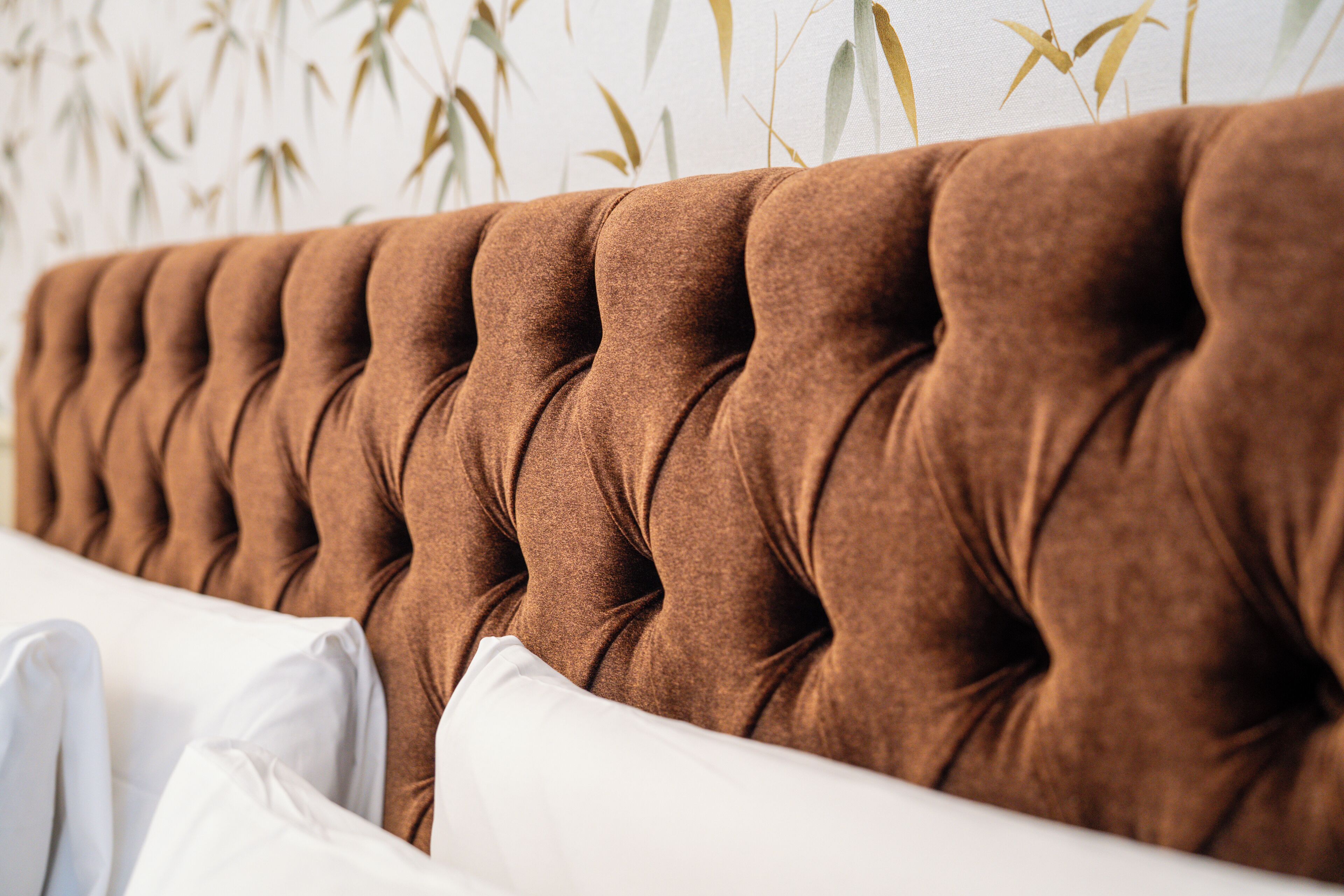 A tufted headboard with a row of buttons, white pillows, and a wall with vertical bamboo patterns.