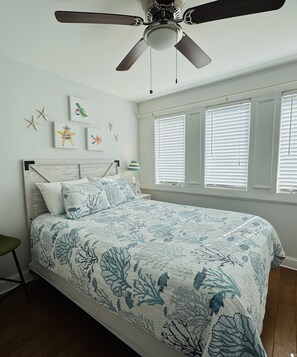 A bedroom with a bed, a ceiling fan, starfish wall art, and a window with blinds. - Nauti on Tybee @ Captains Watch - Pool, 15th St (Tybee Island)