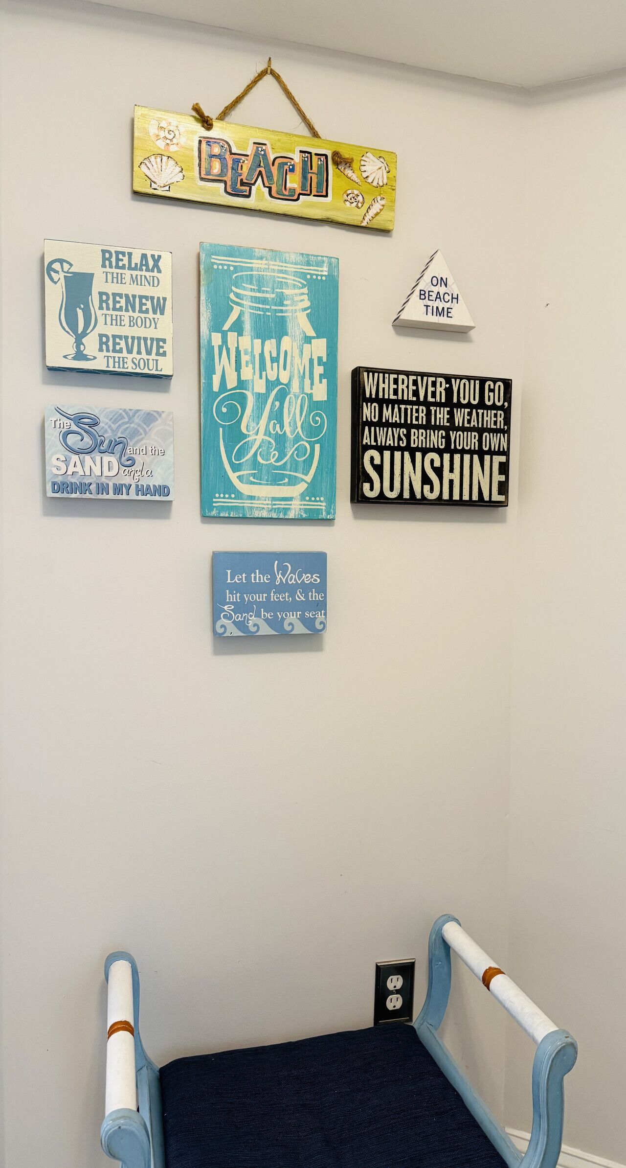 Eine Wand mit verschiedenen motivierenden und strandbezogenen Schildern, einem kleinen Stuhl und einer Steckdose.