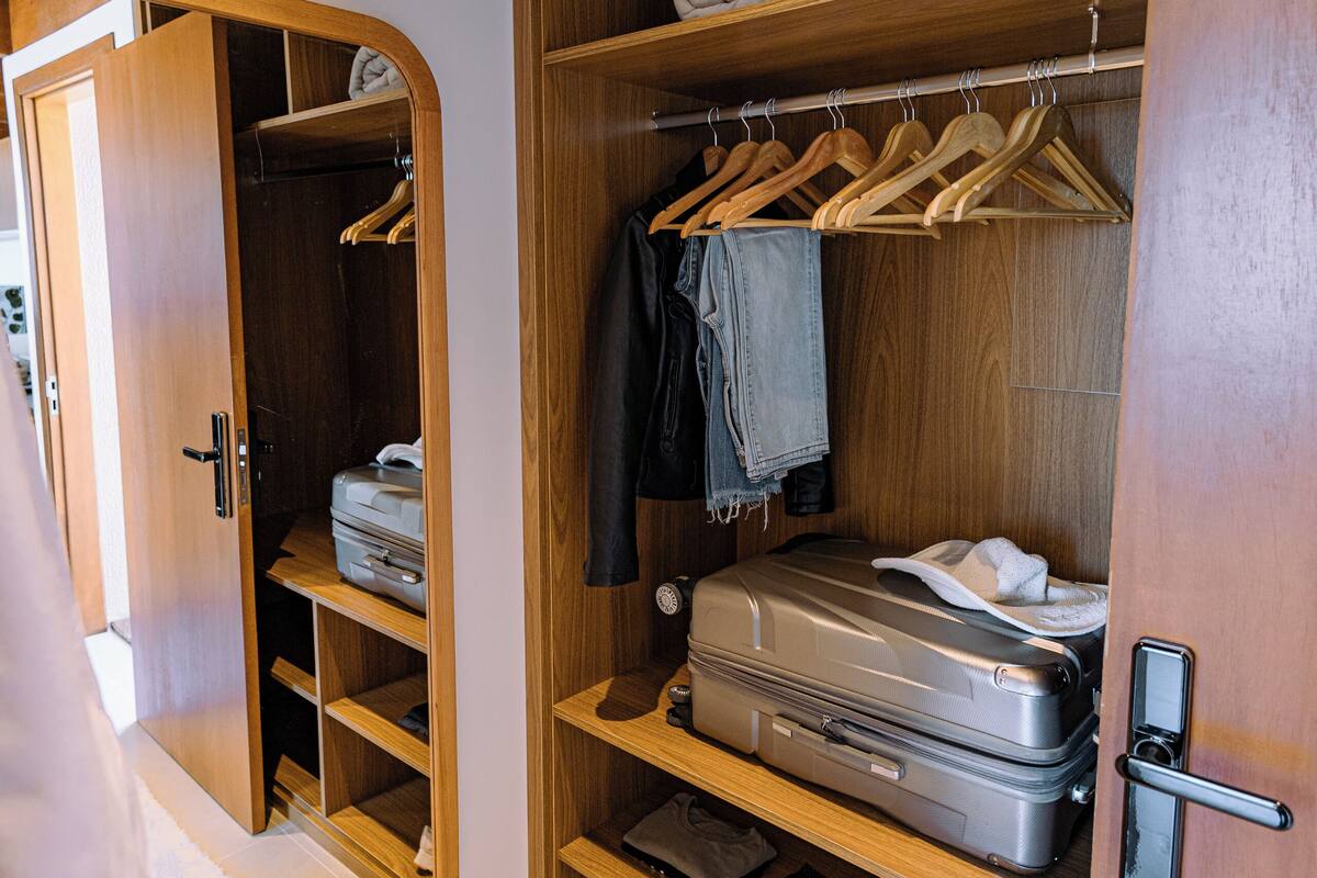 Une armoire en bois avec plusieurs étagères, une tringle pour suspendre les vêtements et un compartiment pour valise.