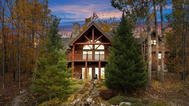 Eine Blockhütte mit einem Steinkamin, umgeben von einem Wald und einem kleinen Teich.