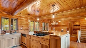 Eine Holzblockhausküche mit Holzausstattung, einer zentralen Kochinsel und großen Fenstern.