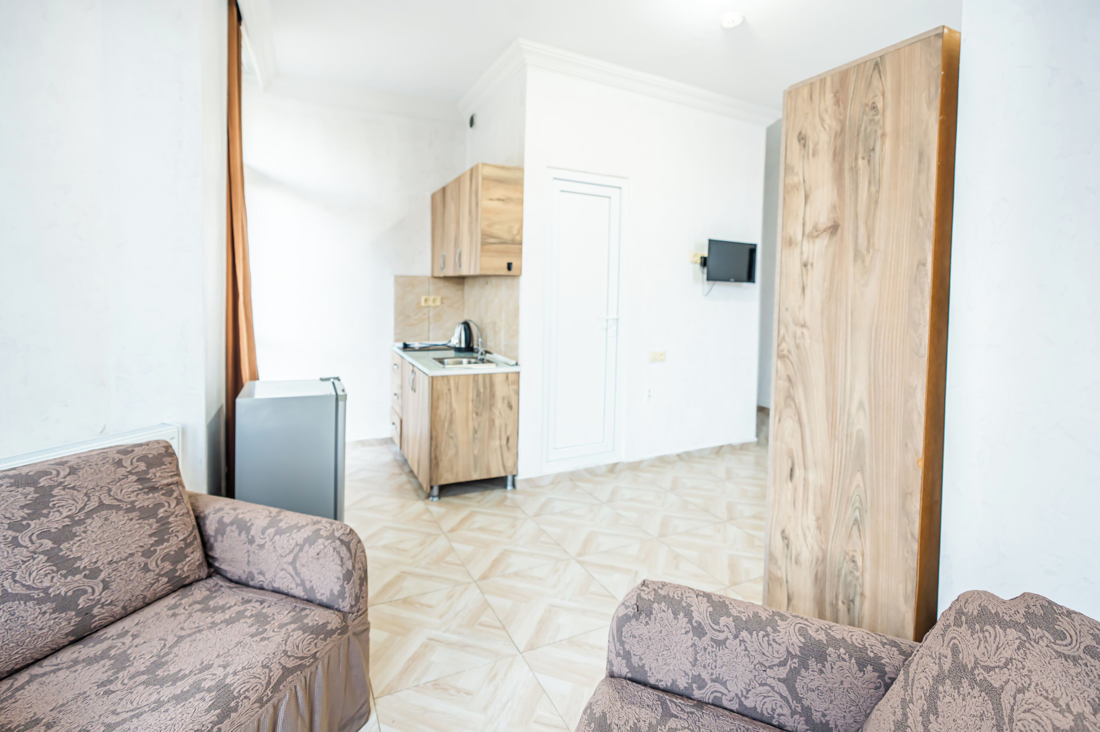 A modern living room with patterned sofas, a kitchen in the background, and a wooden partition.