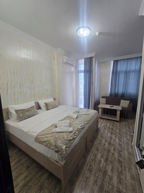 A hotel room with a large bed, a bedside table, a sofa, and a window with curtains. - Batumi Inn (Batumi)