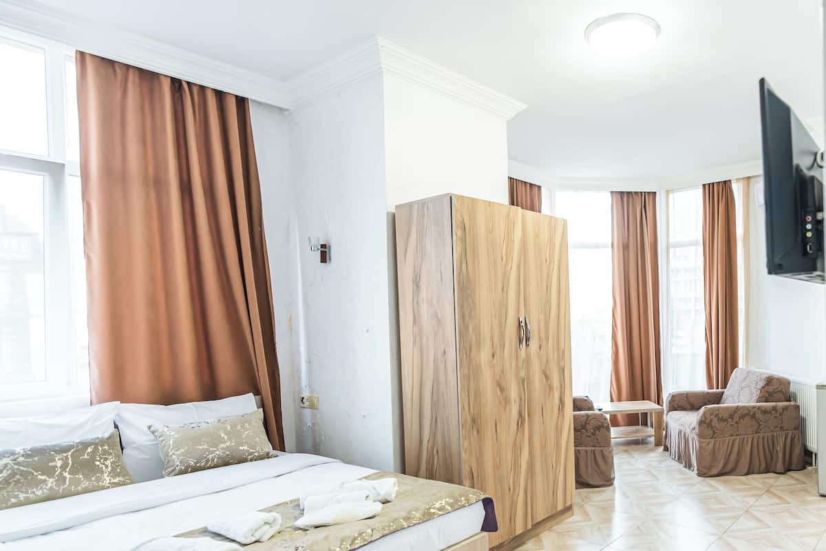 Hotellihuone, jossa on sänky, vaatekaappi, oleskelualue ja televisio.