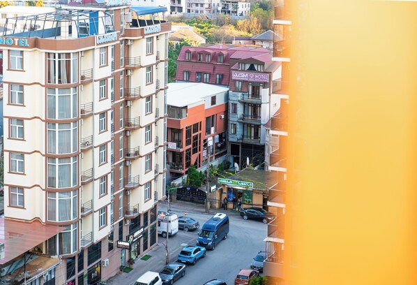 A multi-story hotel with balconies, a central courtyard, and a street view with parked cars and a bus. - Batumi Inn (Batumi)