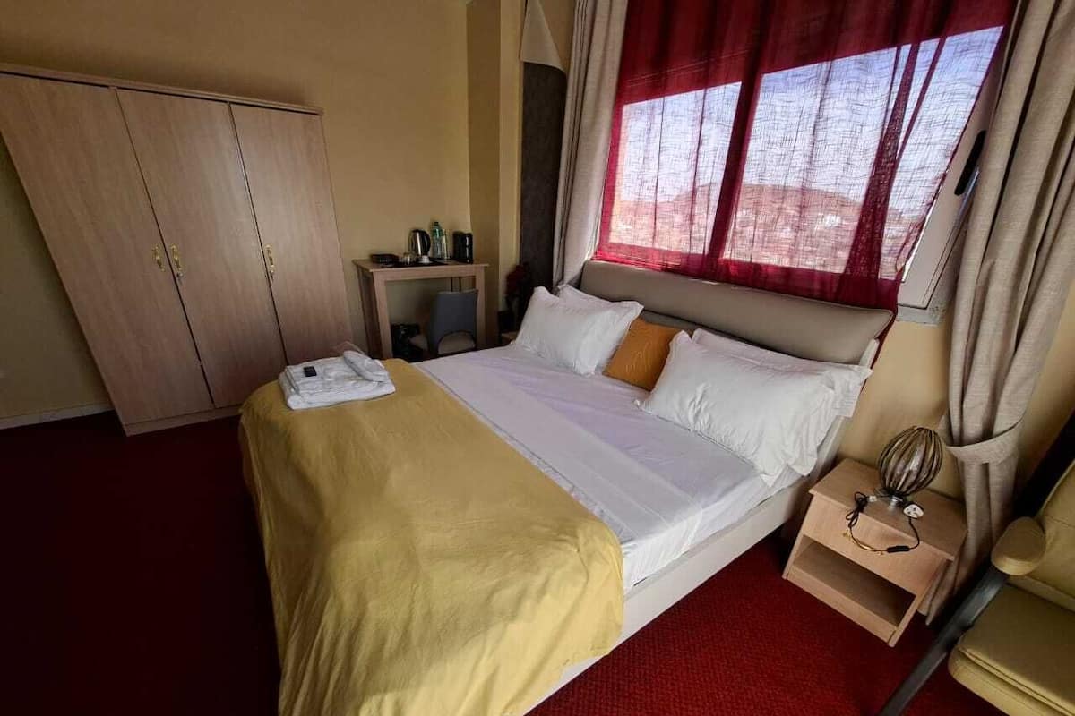 Een hotelkamer met een bed, nachtkastje, kledingkast en een raam met gordijnen.