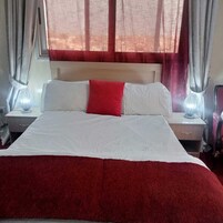 Una cama con ropa de cama blanca y roja, dos lámparas de noche y una ventana con cortinas rojas.