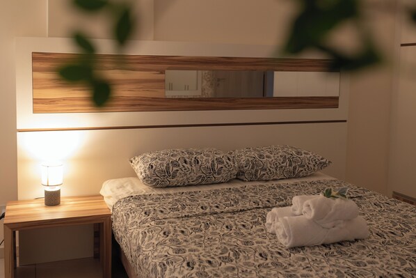 Een netjes opgemaakt bed met beddengoed met een patroon, een bedlampje en een opgevouwen handdoek op het nachtkastje.