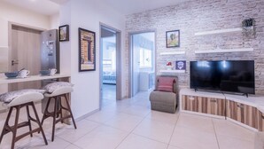 Un salon moderne avec un mur en pierre, un téléviseur à écran plat et un coin cuisine équipé de tabourets de bar.
