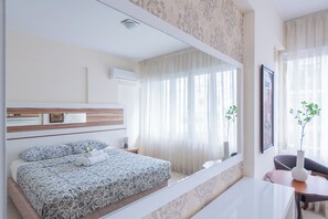 Een moderne slaapkamer met een groot bed, een nachtkastje, een spiegel en een raam met dunne gordijnen.