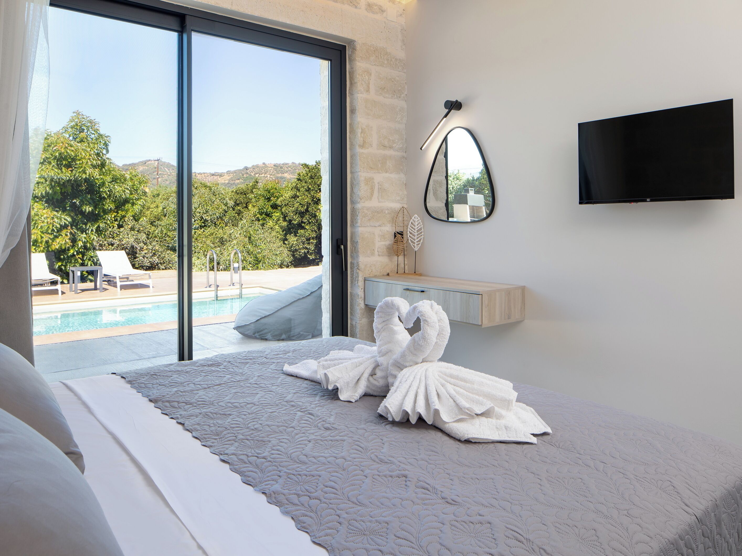 A bedroom with a large bed, a view of a swimming pool, and a mounted TV.