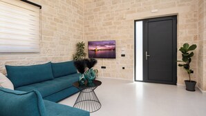 Ein modernes Wohnzimmer mit einem türkisfarbenen Sofa, einem schwarzen Couchtisch und einem Fernseher an einer Ziegelwand.