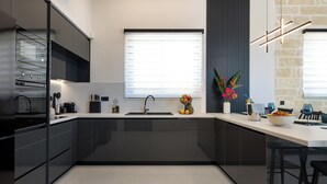 Eine moderne Küche mit dunklen Schränken, einem Einbauofen, einem Spülbecken und einem Fenster mit Jalousien.