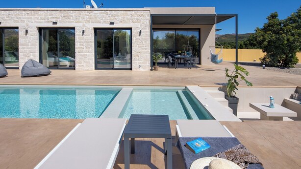 Ein modernes Haus mit Swimmingpool, Sitzgelegenheiten im Freien und einer Terrassenfläche.