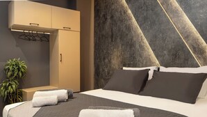 Ein modernes Hotelzimmer mit einem großen Bett, einer dunkel strukturierten Wand und einem kleinen Nachttisch mit einer Pflanze.