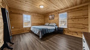 Une pièce de cabane en bois comprenant un lit, un téléviseur et une fenêtre.