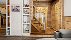 Une pièce chaleureuse avec un escalier en bois, un mur en briques blanches agrémenté d’étagères et un canapé gris.