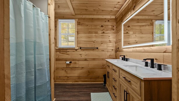 Une salle de bain rustique, avec des murs en bois, un grand miroir, deux lavabos et une fenêtre.