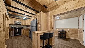 Une cuisine en bois avec un îlot central, des tabourets de bar noirs, un réfrigérateur et un four à micro-ondes.