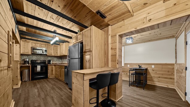 A wooden kitchen with a central island, black bar stools, a refrigerator, and a microwave. - Cozy Cabin Feel • Large Yard • Dog Friendly • Bar (McKees Rocks)