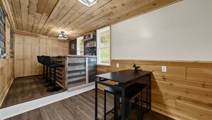 A wooden interior with a bar area, stools, a table, and a window with blinds. - Cozy Cabin Feel • Large Yard • Dog Friendly • Bar (McKees Rocks)
