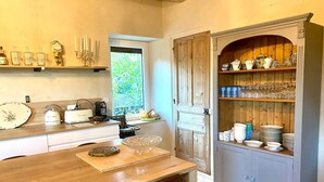 Una cocina acogedora con una mesa de madera, una cafetera y un armario con vajilla y vasos.