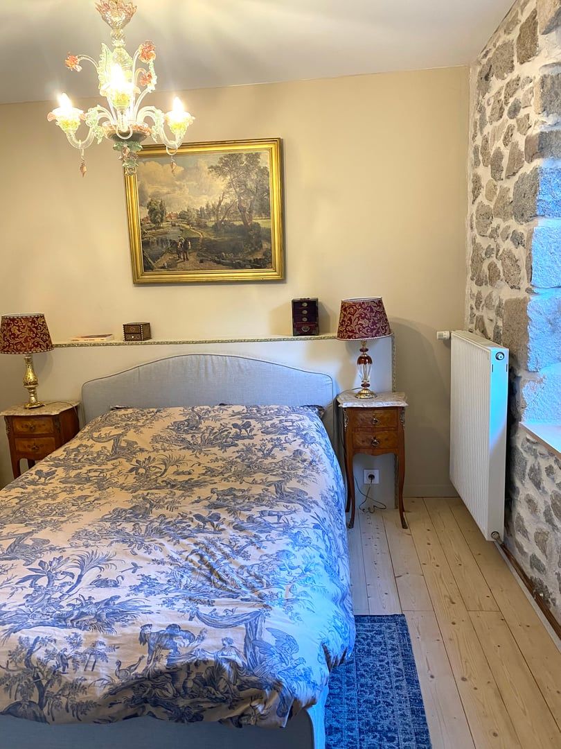 Un dormitorio con cama, candelabro, cuadro, pared de piedra y radiador.
