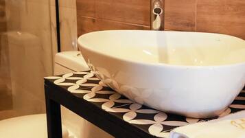 A bathroom with a white vessel sink, a toilet, and a shower area.