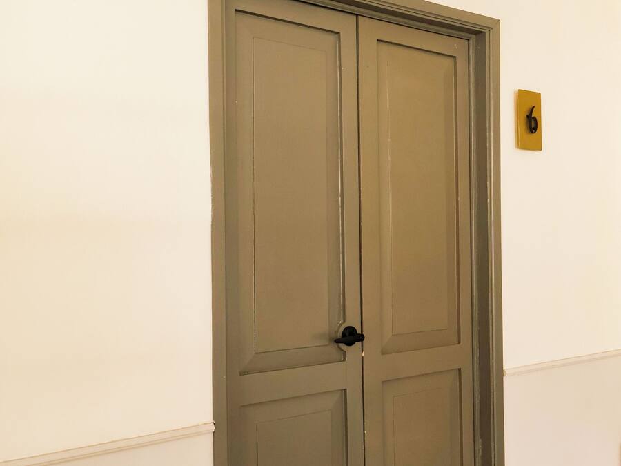 Una porta doble tancada amb un pom negre, una làmpada de paret i una placa petita amb el símbol d'un telèfon.