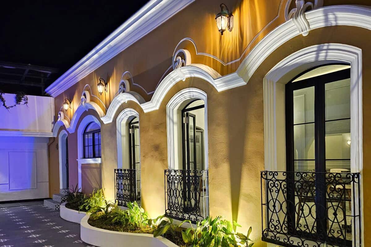 Un edificio con ventanas de arco, iluminación decorativa, entrada de baldosas y una jardinera con follaje.