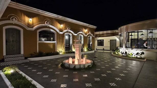 Un patio con una fuente central, suelo de baldosas y un edificio con ventanas de arco y un balcón.