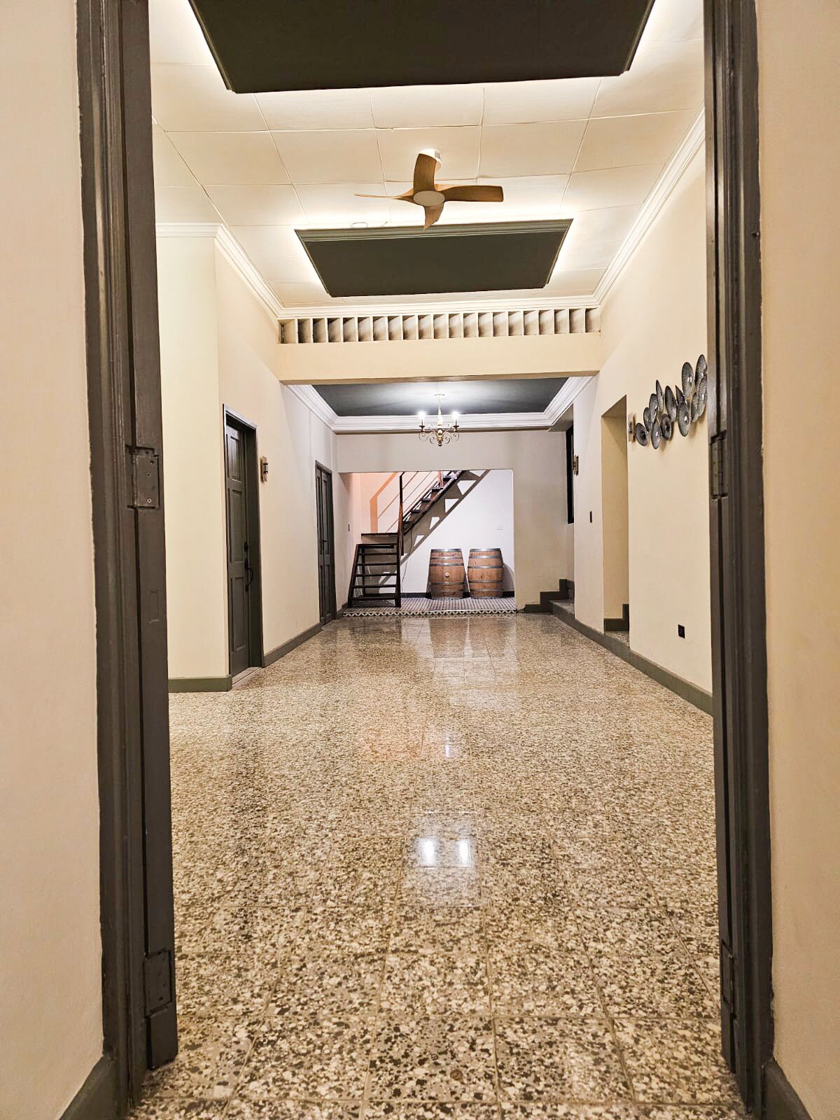 A spacious hallway with a polished stone floor, a ceiling fan, and a staircase leading to an upper level.