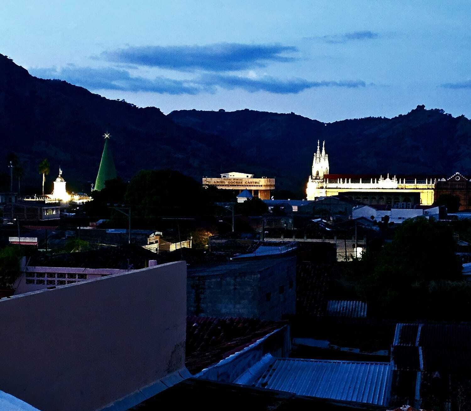 A cityscape at dusk with illuminated buildings, including a church with a spire and a building labeled "Angel Gocorrez Castro."