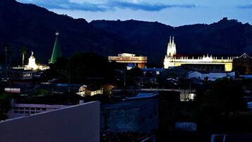 Un paisaje urbano al atardecer con edificios iluminados, incluyendo una iglesia con aguja y un edificio que dice "Angel Gocorrez Castro".