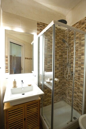 A bathroom with a glass-enclosed shower, a sink with a mirror above, and a wooden cabinet below. - SuiteHouse78 - Elegant, centrally located apartment with a private garden, near Bari's Old Town (Bari)