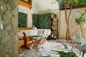 A stone-walled patio with a table and chairs, a wooden bookshelf, and a hanging plant. - SuiteHouse78 - Elegant, centrally located apartment with a private garden, near Bari's Old Town (Bari)