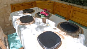 A dining area with a stone wall, wooden cabinets, and a table set for four with plates, glasses, and a basket of flowers. - SuiteHouse78-Elegant Central Apartment with Private Garden, near Bari Old Town (Bari)