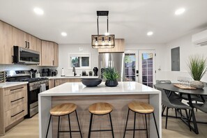 A modern kitchen with a central island, bar stools, stainless steel appliances, and a dining area with a table and chairs. - Modern 6BR Lynnwood Retreat w/ AC • 2 Full Chef Kitchens • Close to Downtown (Lynnwood)