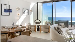 Ein modernes Wohnzimmer mit Essbereich, großen Fenstern und Meerblick sowie minimalistischer Einrichtung.