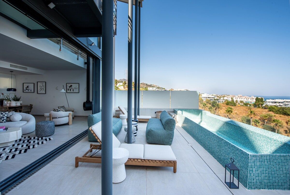 A modern outdoor living space with a pool, lounge chairs, and a view of the coastline.