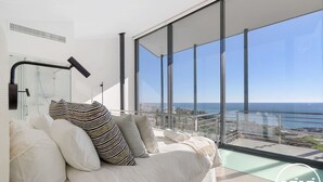 Ein modernes Schlafzimmer mit großem Fenster und Blick auf Stadt und Meer.