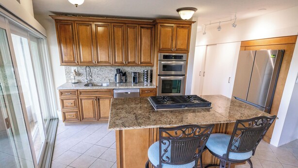 A kitchen with wooden cabinets, stainless steel appliances, a granite countertop, and two bar stools. - Sea Forever Vista - Ocean Views From Every Room - 5 Minutes to Magen's Bay Beach (Mandahl)